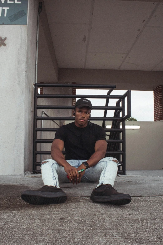 a man sitting on the ground in front of a building, black main color, in style of tyler mitchell, confident stance, maximus jacobs