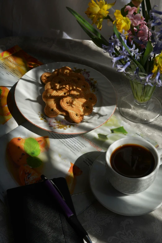 a white plate topped with cookies next to a cup of coffee, a still life, by Alice Rahon, sun flares, easter, angelina stroganova, photographed for reuters