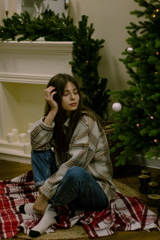 a woman is sitting on the floor in front of a christmas tree