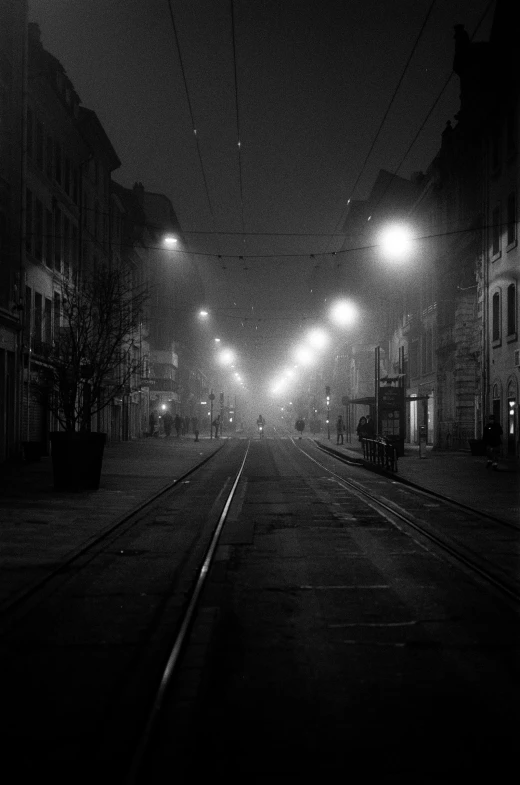 a black and white photo of a street at night, a black and white photo, by Albert Keller, realism, tram, ((mist)), hannover, 8k artistic 1920s photography