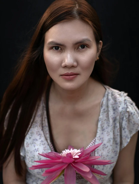 a woman holding a pink flower in front of a black background, inspired by Ruth Jên, looking directly at the camera, thawan duchanee, low quality photo, ((portrait))