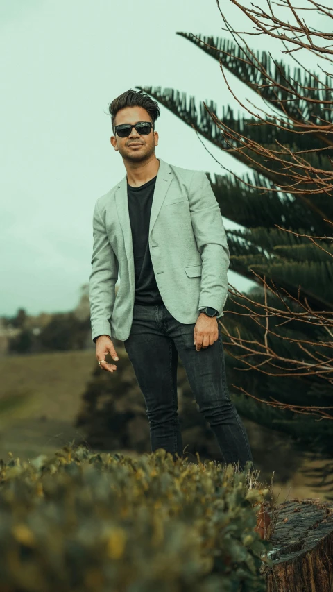 a man stands near a tree with his hands in his pockets