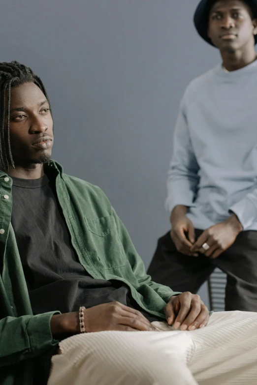 a couple of men sitting next to each other, by Stokely Webster, trending on unsplash, visual art, dreadlock black hair, serious business, wearing a green sweater, at a fashion shoot