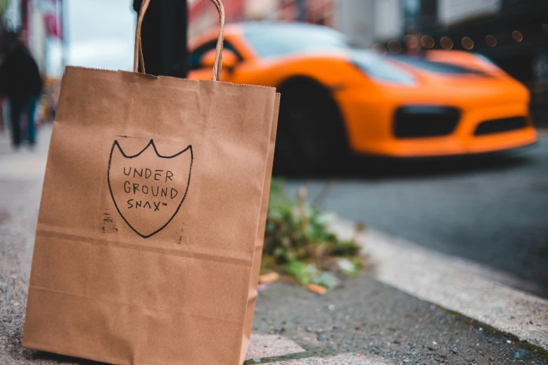 a brown paper bag sitting on the side of a street, sports car in the room, exiting store, underground, logo for lunch delivery