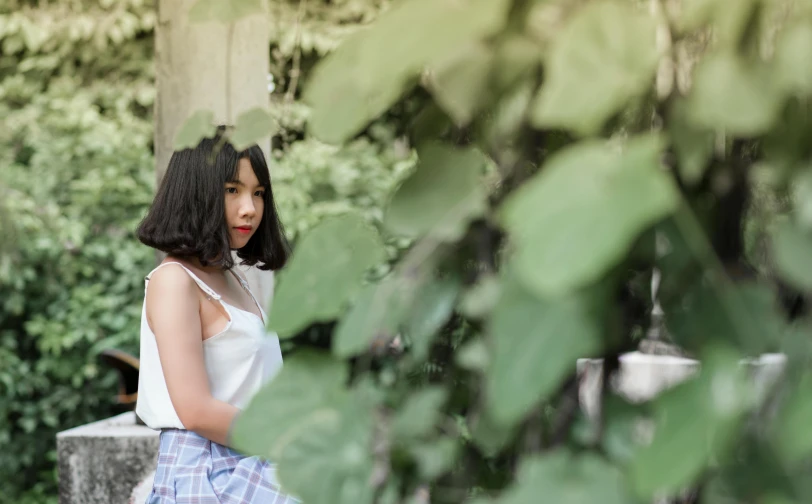 a woman sitting on a bench in a park, inspired by Elsa Bleda, pexels contest winner, black hime cut hair, with ivy, asian girl, white shirt and green skirt