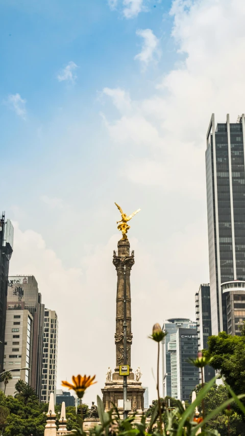 a statue in the middle of a city surrounded by tall buildings, by Alejandro Obregón, pexels contest winner, mexico city, upright, a phoenix, hi-res
