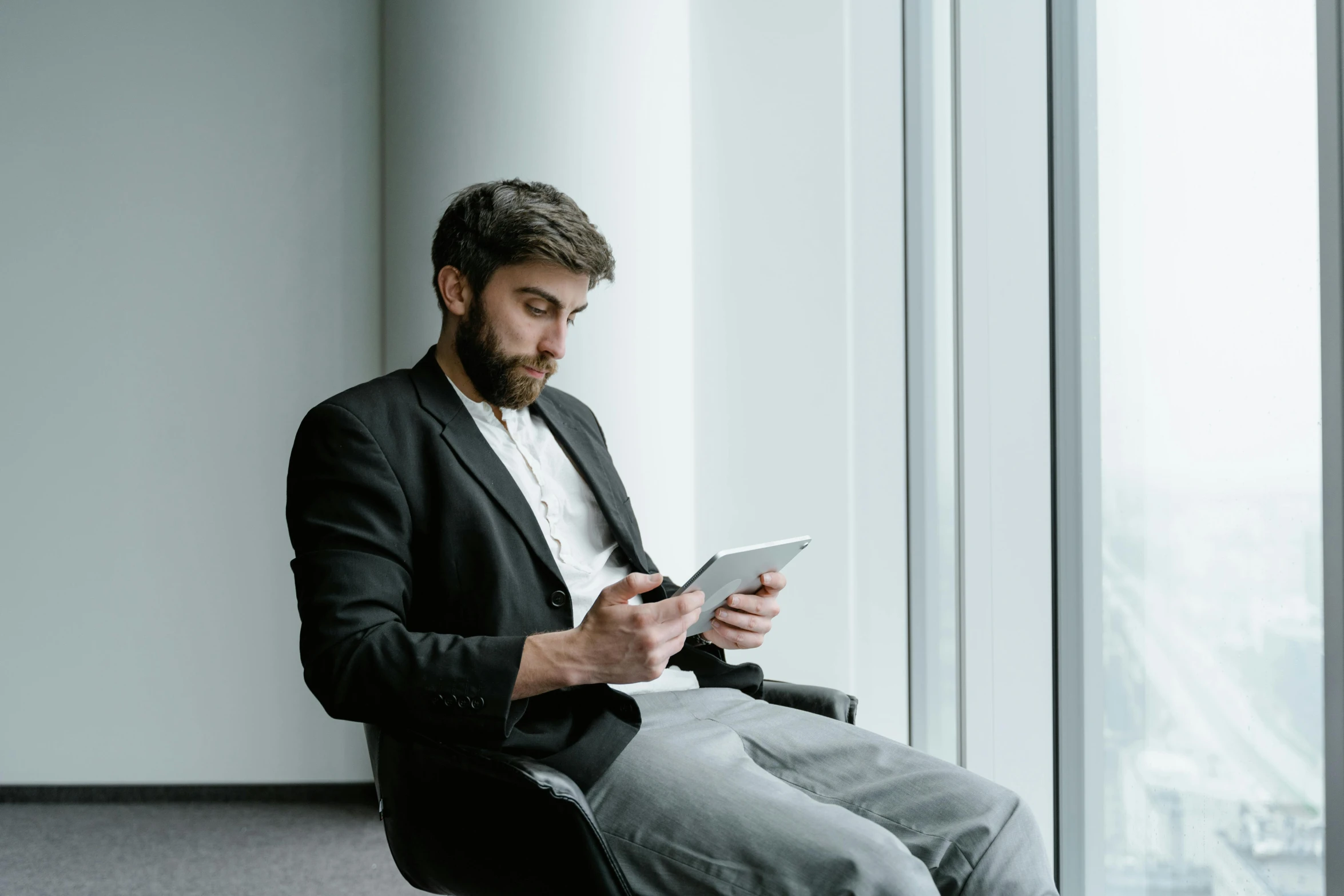 a man sitting in a chair looking at a tablet, pexels contest winner, wearing causal black suits, it specialist, link from zelda using computer, man with beard