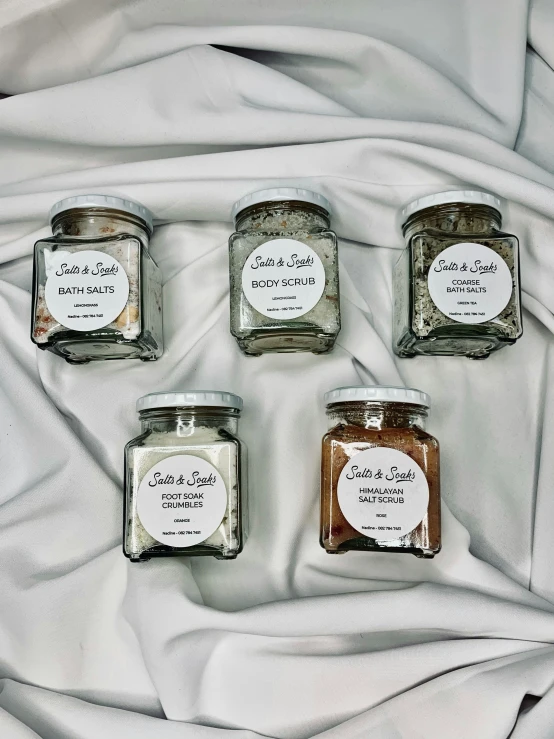 four jars of spices on a white cloth, a portrait, inspired by Eden Box, featured on instagram, bubble bath, 6 pack, detailed product image