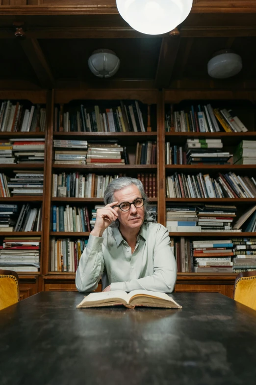 a man sitting at a table with a book in front of him, annie leibowitz, librarian, peter hurley, gray haired