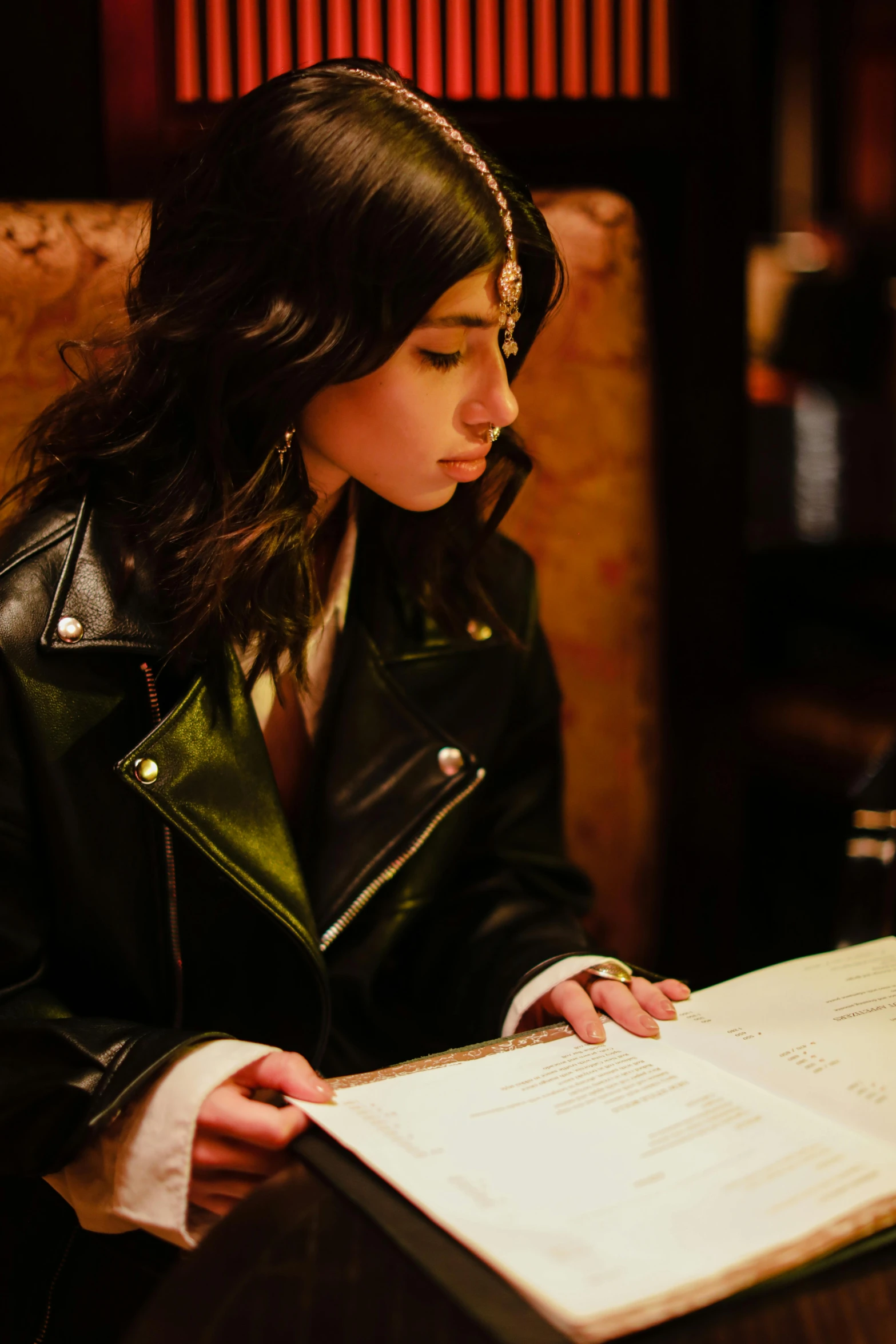 a woman sitting at a table reading a book, an album cover, trending on pexels, dressed in leather jacket, soft lighting, signing a bill, asher duran