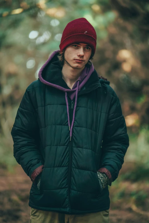 man wearing green coat with maroon hat in woods