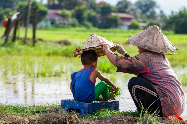 a woman and a child sitting next to a body of water, pexels contest winner, sumatraism, rice paddies, avatar image, square, people at work