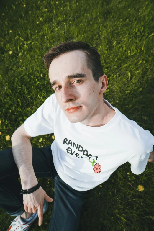 a man sitting on top of a lush green field, an album cover, inspired by Alexander Kanoldt, featured on reddit, realism, wearing a tie-dye t-shirt, large friendly eyes, discord profile picture, embroidered shirt