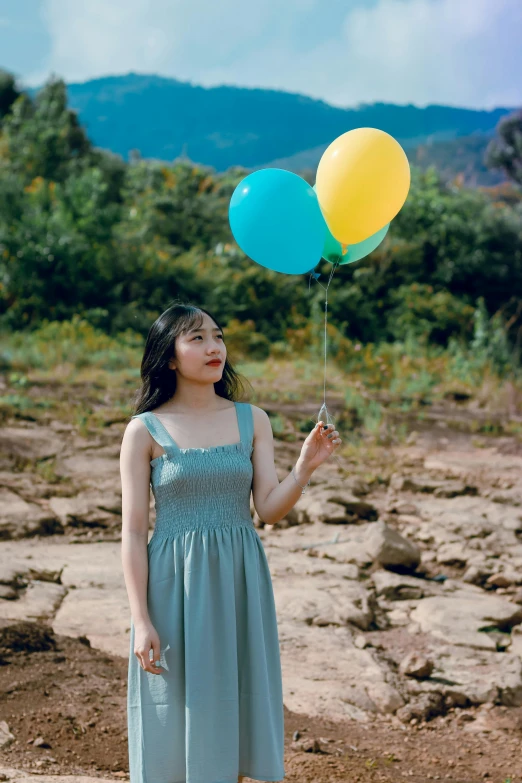 a woman in a blue dress holding two yellow and blue balloons, by Tan Ting-pho, pexels contest winner, korean girl, 256435456k film, wearing a flowing sundress, grey