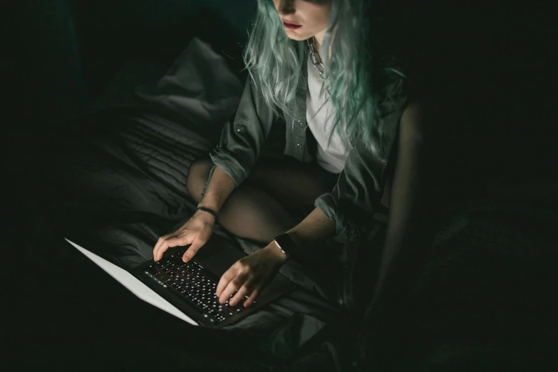 a woman sitting on a bed using a laptop computer, a photo, inspired by Elsa Bleda, trending on pexels, computer art, dark green hair, playing games, underexposed grey, discord profile picture