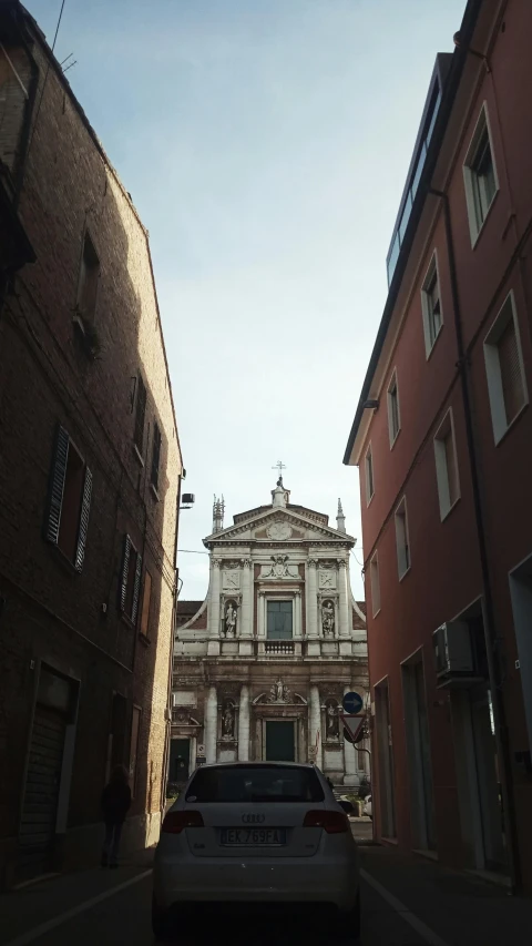 a car driving down a narrow street next to tall buildings, an album cover, by Canaletto, pexels contest winner, renaissance, church, symmetrical front view, brown, palladian