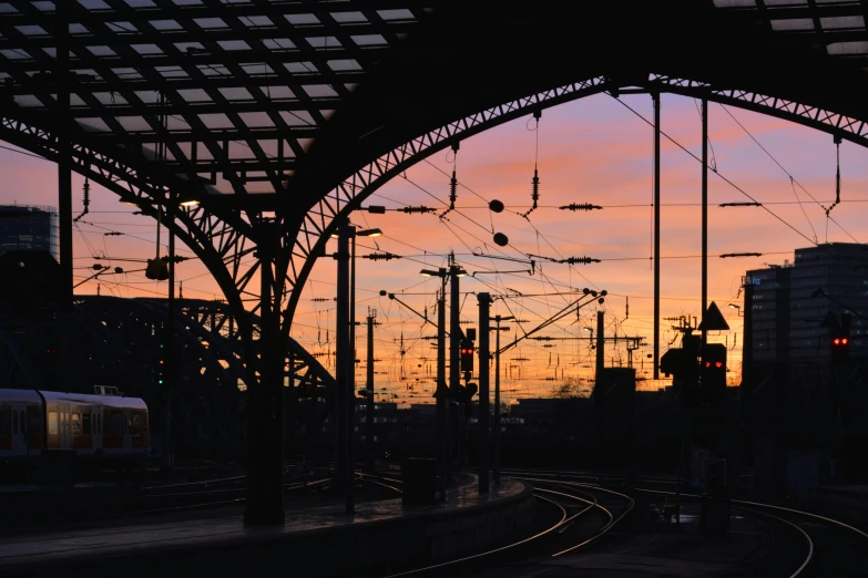 a train traveling through a train station next to tall buildings, by Kristian Zahrtmann, pexels contest winner, silhouette over sunset, pink arches, hannover, electricity archs