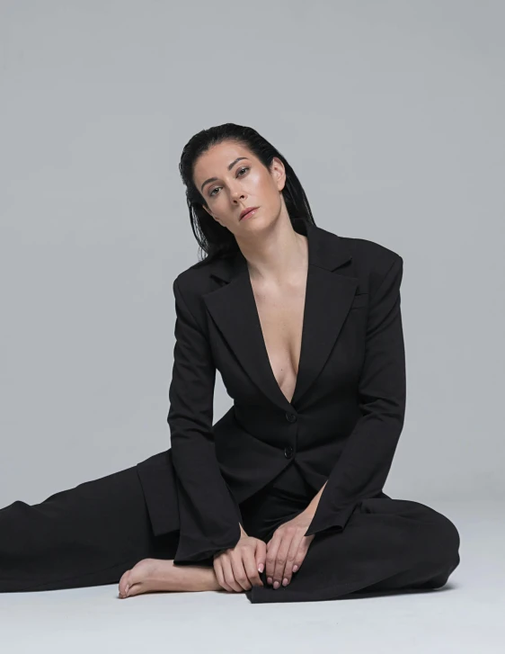 a woman in a black suit sitting on the floor, an album cover, inspired by Marina Abramović, unsplash, slicked black hair, nonbinary model, neri oxman, doing an elegant pose over you