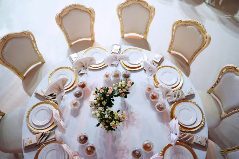 a dining room table is set with gold trimmed chairs and a white clothed table