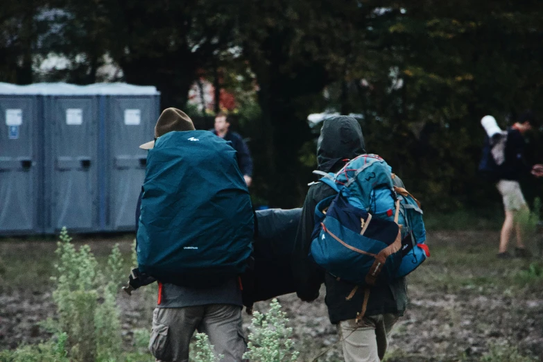 a couple of people with backpacks walking through a field, by Emma Andijewska, happening, portapotty, lit from behind, dingy, cinematic