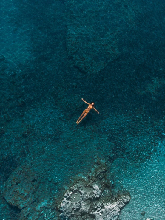 a person on a surfboard in the middle of a body of water, coral sea bottom, top down, overlooking the ocean, lying down