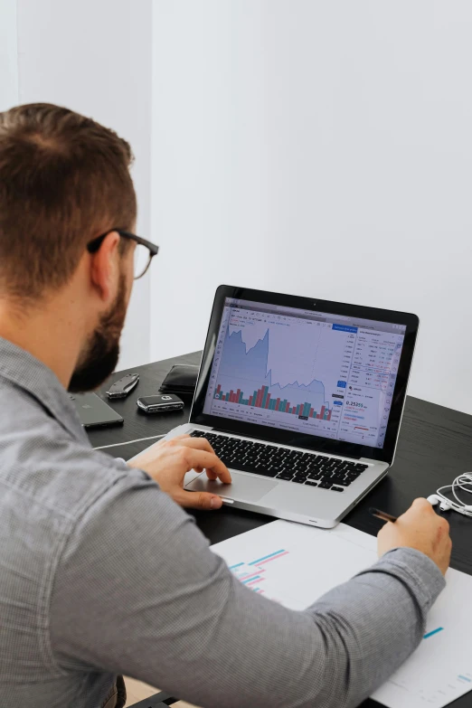 a man sitting at a desk working on a laptop, a computer rendering, by Jay Hambidge, trending on unsplash, graphs, trading, official screenshot, grey