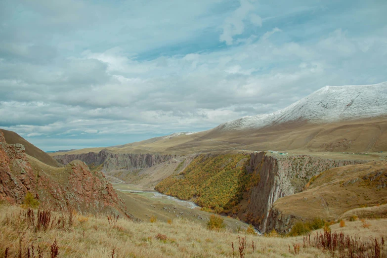 the view of mountains, grass and flowers with a river running through them