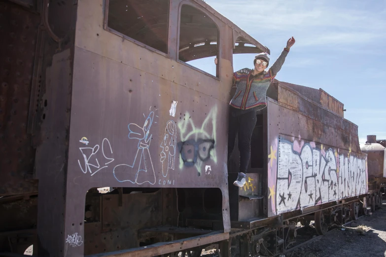 a man standing on top of a train covered in graffiti, a portrait, inspired by Banksy, unsplash, graffiti, girl with warship parts, waving at the camera, some rust, lachlan bailey