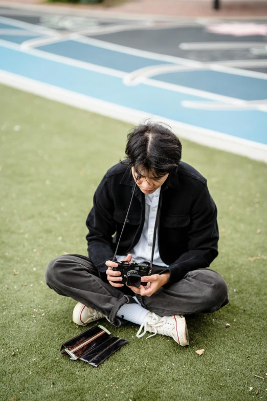 a man sitting on the ground holding a camera, kentaro miura style, on a football field, high-quality photo, fujifilm”