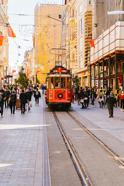 a red trolley traveling down a street next to tall buildings, by Niyazi Selimoglu, pexels contest winner, ottoman empire, busy streets filled with people, light tan, gif