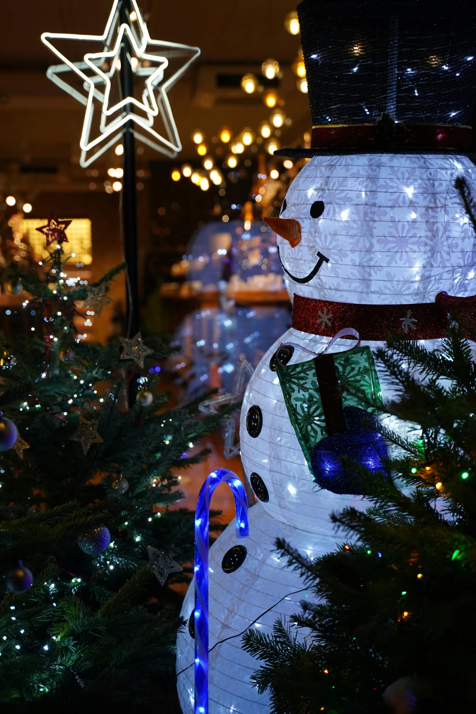 a lit up snowman next to some christmas trees