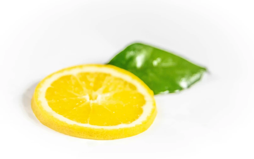 a slice of lemon next to a leaf on a white surface, a picture, by Gavin Hamilton, pexels, made of glazed, high quality product image”, circle, infused