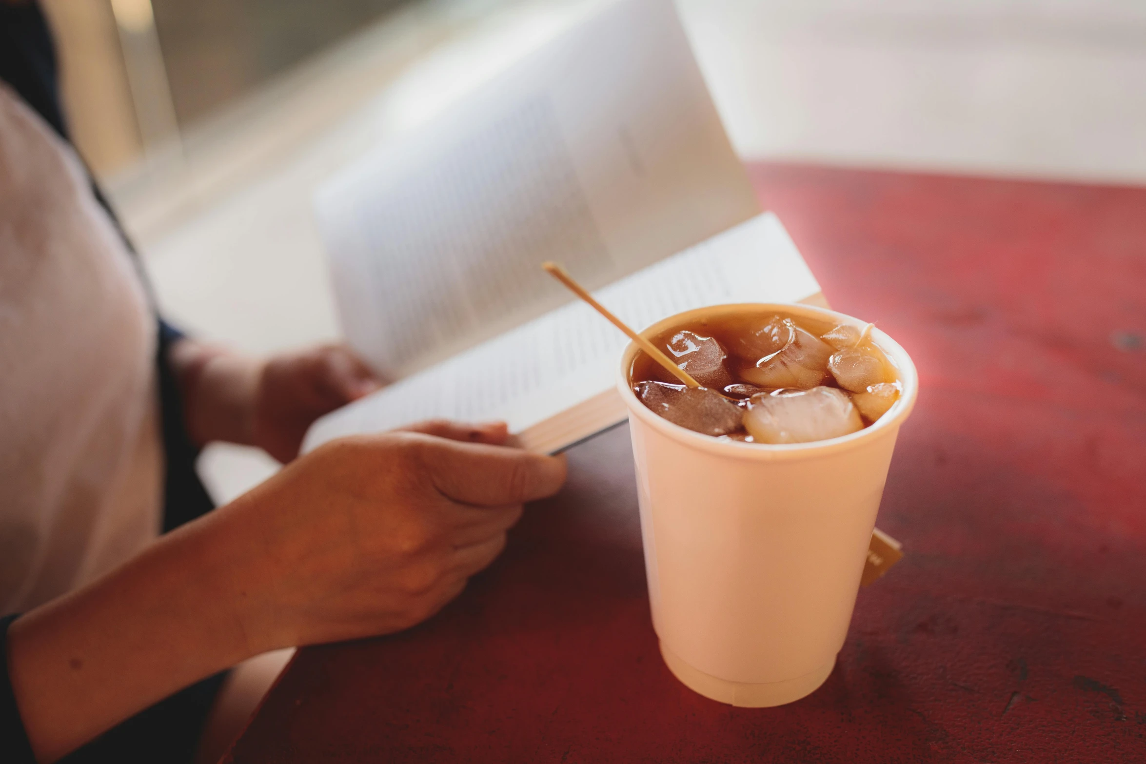 a person sitting at a table with a book and a cup of coffee, with a straw, cold brew coffee ), 15081959 21121991 01012000 4k, press shot