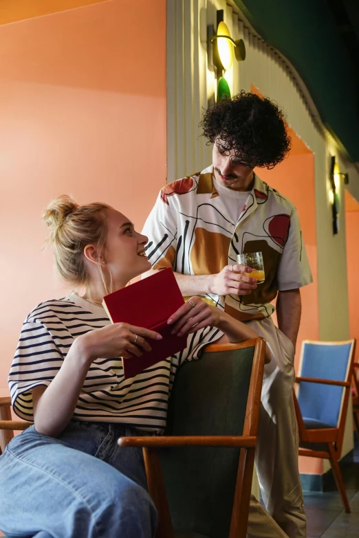 a woman sitting in a chair next to a man reading a book, people drink cocktails, charli bowater and artgeem, college students, striped