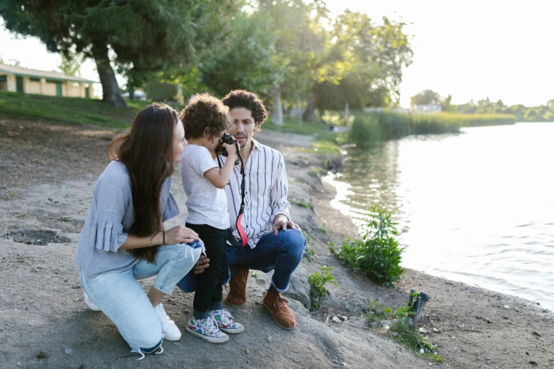 a group of people sitting next to a body of water, pexels contest winner, plein air, portrait of family of three, phone photo, camera flash, of a family standing in a park