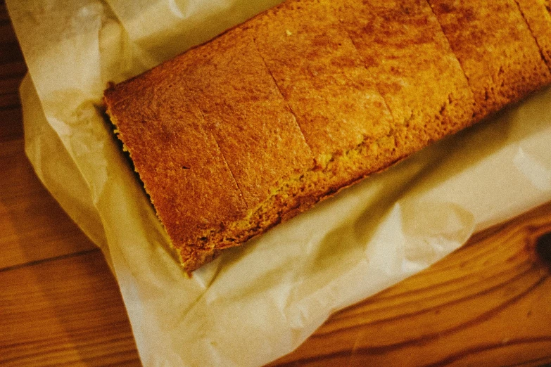 a loaf of bread sitting on top of a wooden table, an album cover, unsplash, detailed texture, yellow, cake, thick lining