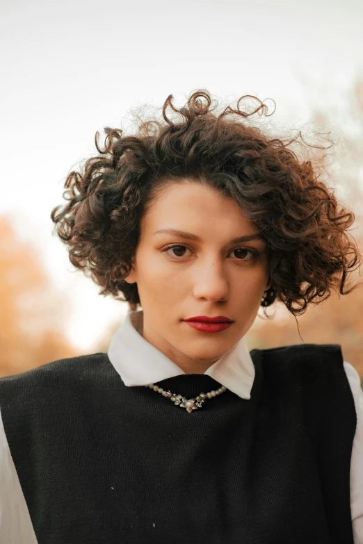 a woman with curly hair wearing a black vest, gal yosef, lapel, androgynous person, square