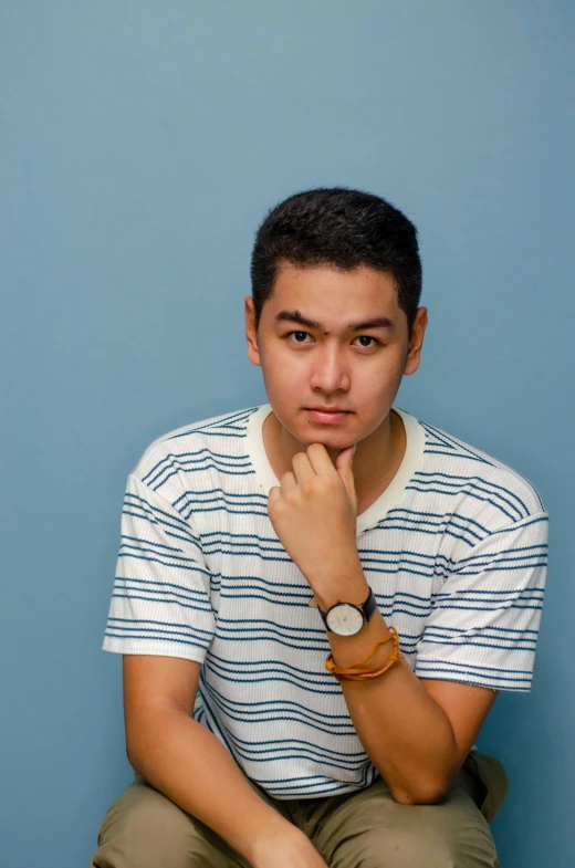 a young man sits in front of a blue background while posing for the camera