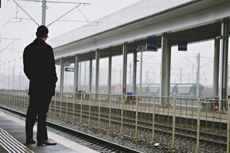 a man waiting for a train at a train station, by Lucia Peka, unsplash, tgv, fan favorite, **cinematic, rectangle