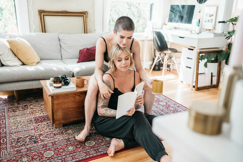 a woman sitting on the floor next to a man, by Julia Pishtar, pexels contest winner, lesbian embrace, reading nook, tattooed, accompany cory chase