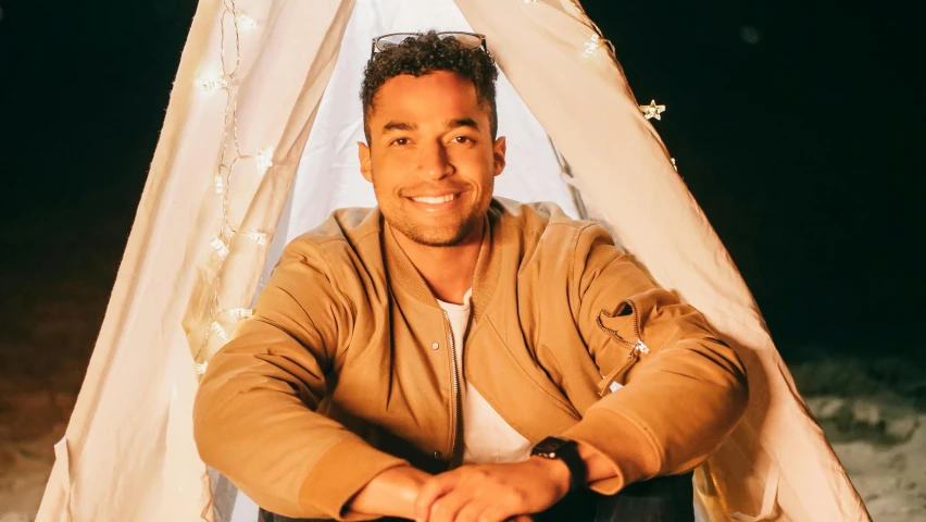 a man that is sitting in front of a tent, holiday vibe, portrait of danny gonzalez, promo image, lean man with light tan skin