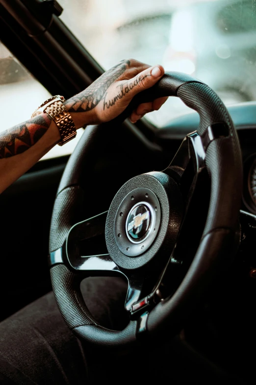 a man sitting in the driver's seat of a car, a tattoo, inspired by Harry Haenigsen, trending on pexels, playboi carti, single steering wheel, alfa romeo giulia, wiz khalifa