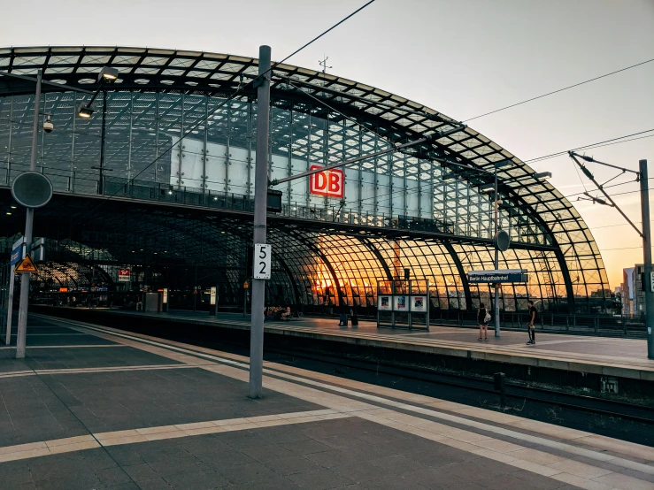 a train station with a train pulling into the station, by Kristian Zahrtmann, pexels contest winner, steel archways, late summer evening, profile image, germany. wide shot
