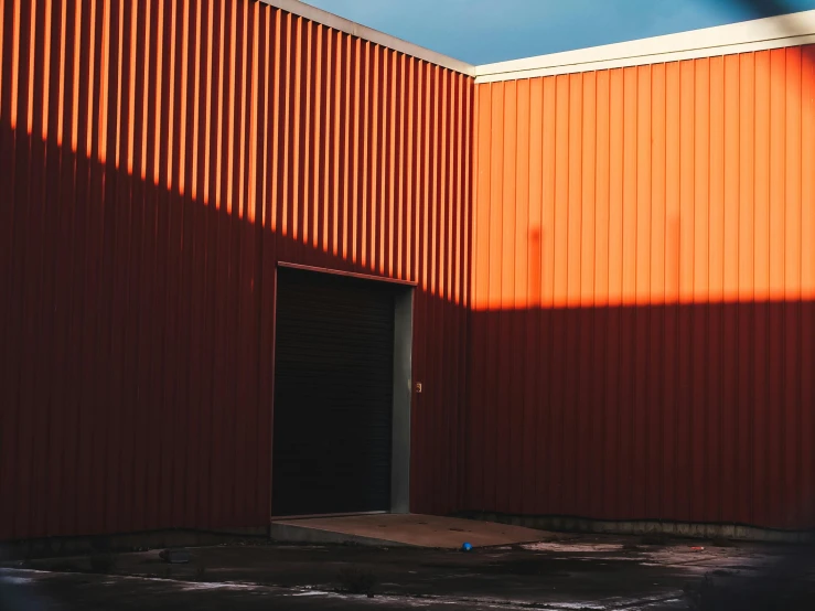 a red building with a blue sky in the background, a photo, inspired by Elsa Bleda, hangar, late afternoon sun, dark grey and orange colours, commercial