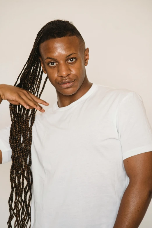 a man standing in front of a white wall, an album cover, inspired by Terrell James, trending on pexels, complex braided hair, non binary model, concert photo, nubian