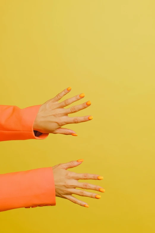 a woman in an orange jacket with her hands in the air, an album cover, inspired by Elsa Bleda, trending on pexels, aestheticism, nail polish, colors: yellow, single pair of hands, h3h3