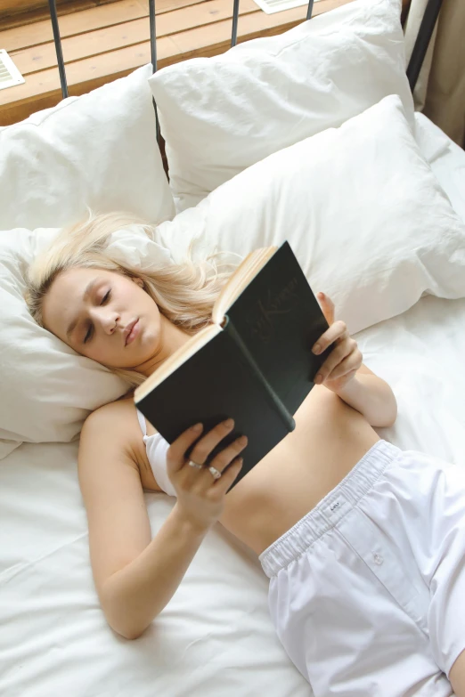 a woman laying in bed reading a book, reddit, blonde women, multiple stories, full frontal shot, high resolution