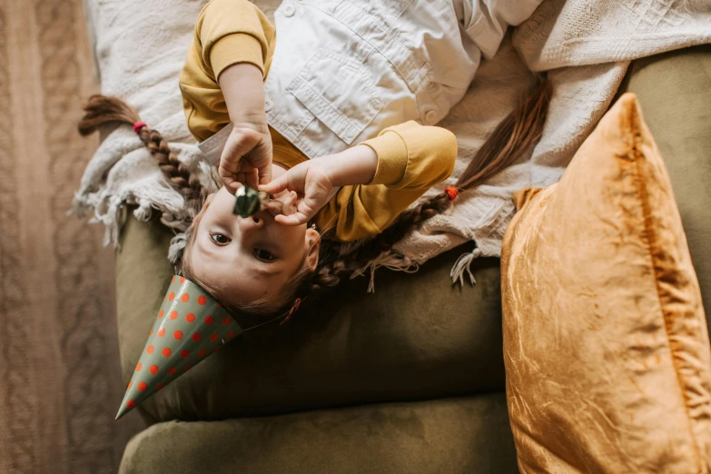 a small child laying on top of a couch, by Emma Andijewska, pexels contest winner, party hats, eating, cottagecore hippie, 15081959 21121991 01012000 4k