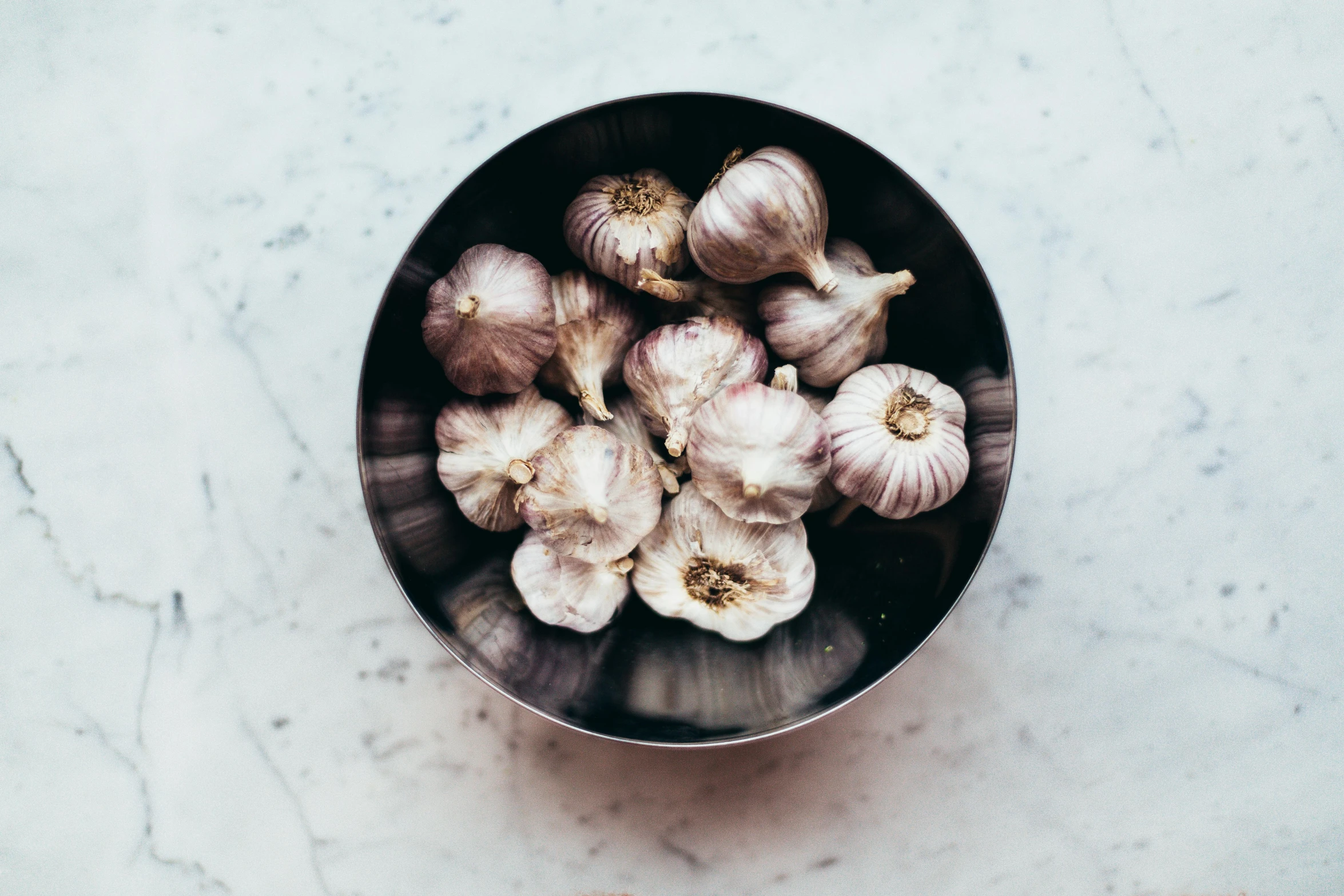 a bowl filled with garlic on top of a table, by Carey Morris, trending on unsplash, stainless steel, grey, multicoloured, all marble