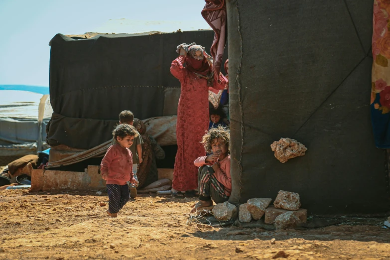 a group of people that are standing in the dirt, by Ibrahim Kodra, pexels contest winner, hurufiyya, makeshift house, mediterranean, families playing, dressed in a worn